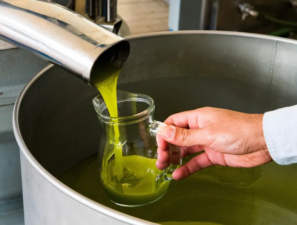 Green liquid being poured from a metal container into a glass jar by a person.